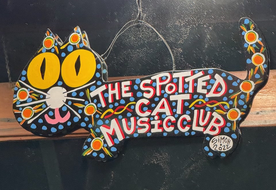 The hand-painted 'Spotted Cat Music Club' sign — a folk-art spotted cat, signed by the artist Simon — in the window on Frenchmen Street, New Orleans.